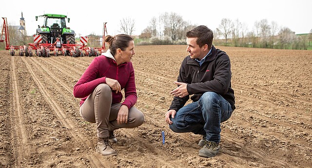 Farmers and crop advisors talk while squatting in the field 